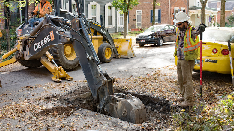 Public works employees using an excavator to dig up part of a residential street.