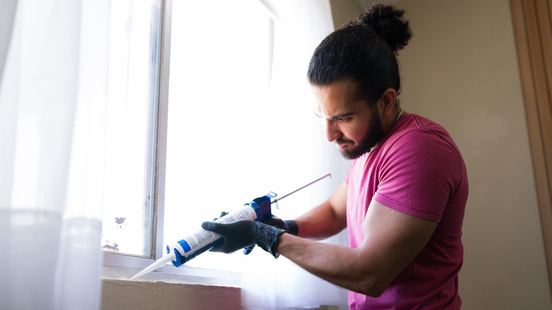 A person carefully applies caulk into a gap near a windowsill in a home