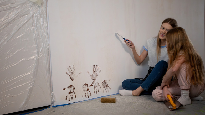 A woman and a girl talking next to a wall that includes handprints of paint near the floor.