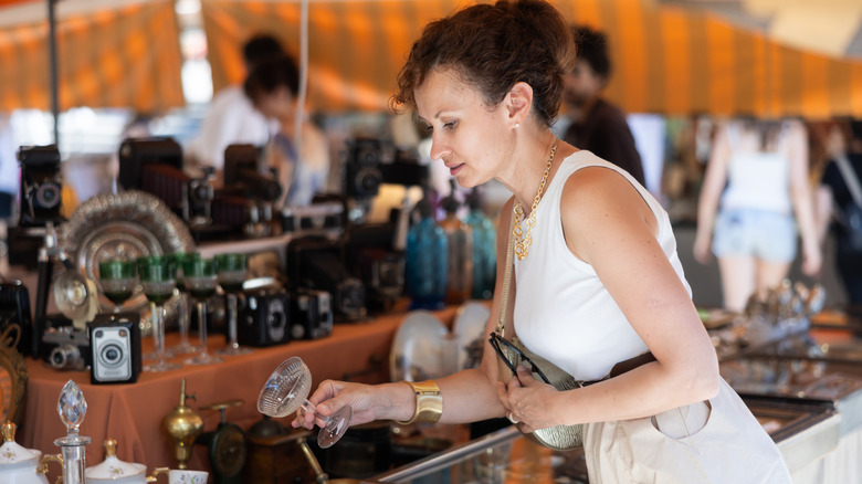 A woman in a white shirt and gold jewelry examining a small glass at an antique market