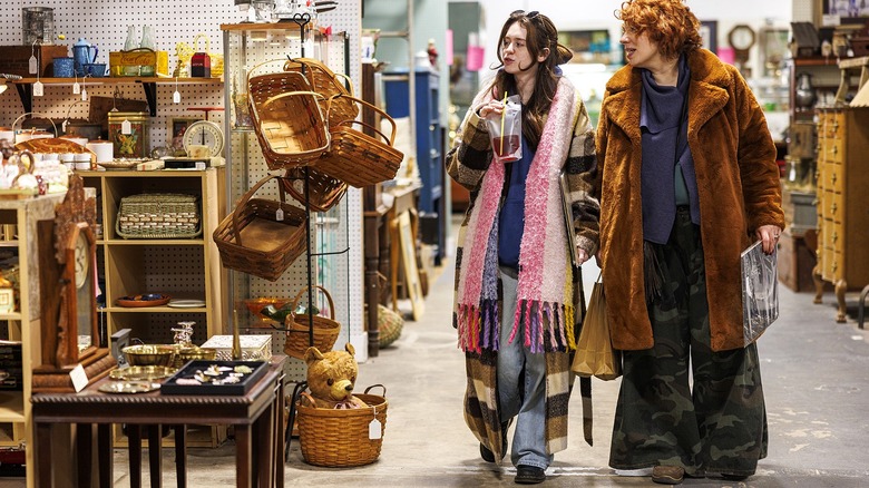 Two people walk through a thrift store near a display of basket and other décor