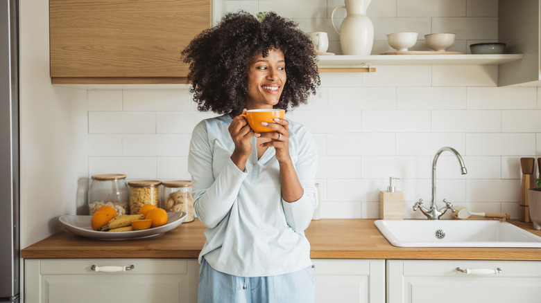 A woman holding a cup of coffee while leaning on kitchen counter.
