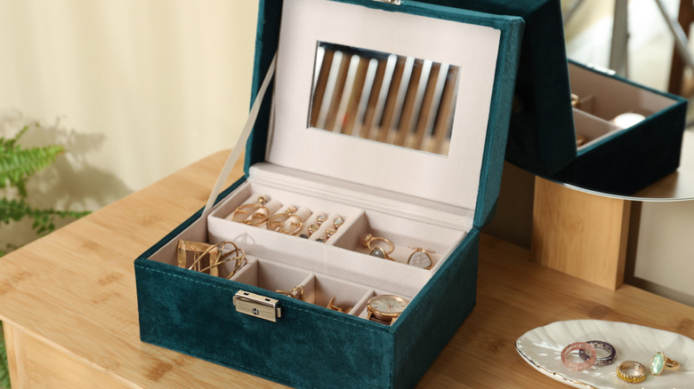 Green velvet jewelry box on table with rings, earrings, and accessories inside.