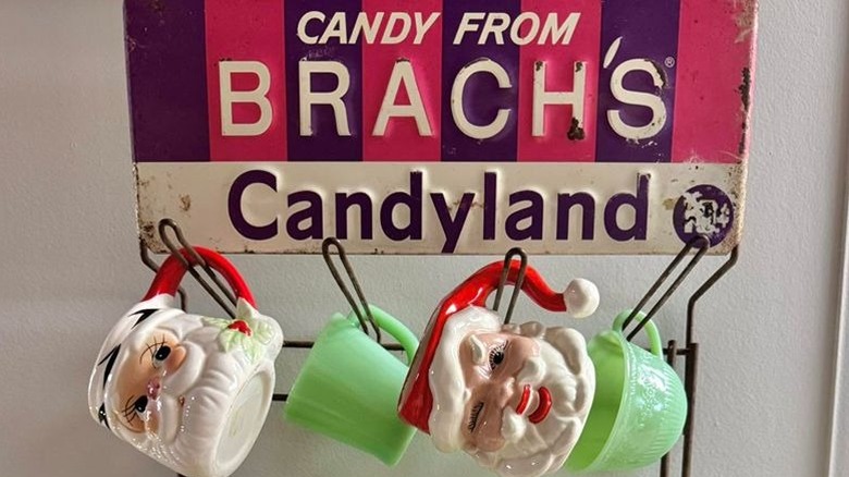 Vintage Brach's candy "Candyland" display being used to hang vintage kitschy Santa mugs with Fire king mugs