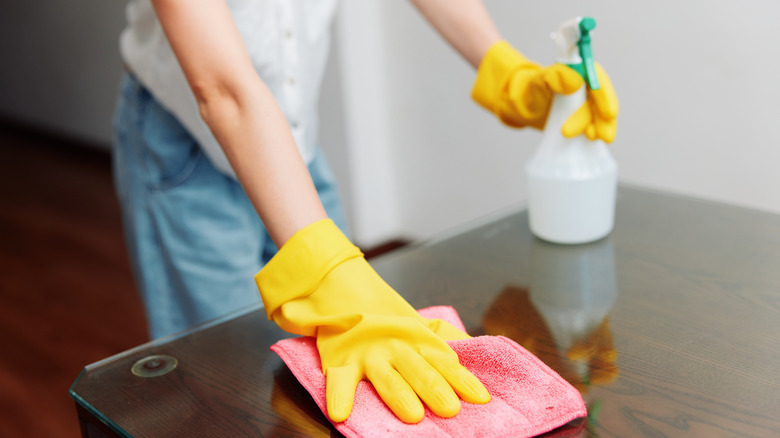 Person cleaning a table with towel and solution