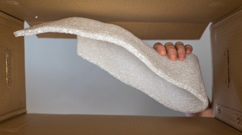 Man's hand holding polyethylene foam in a cardboard box.