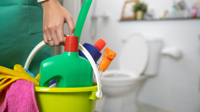 Someone holding a bucket of cleaning supplies in a bathroom