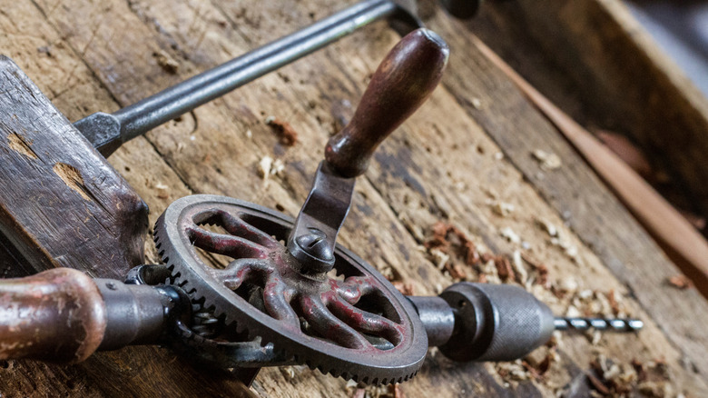 A vintage hand-cranked drill on a workbench.