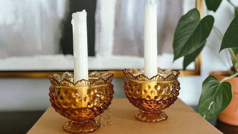 Two hobnail amber glass candle holders holding white tapers, arranged on a book
