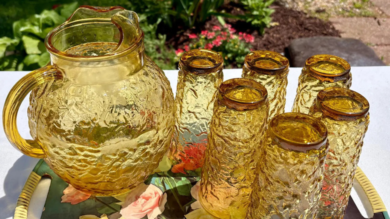 An vintage Anchor Hocking Lido amber drink set with textured glass sits on a patio table with a garden in the background