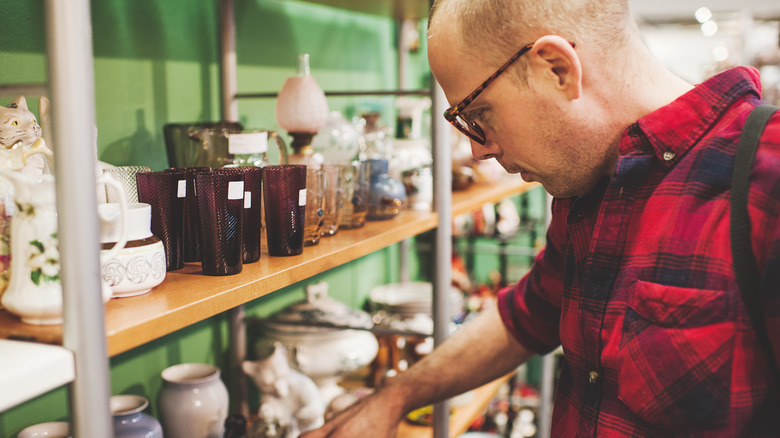 A man looking through thrift store glasses and ceramic pieces