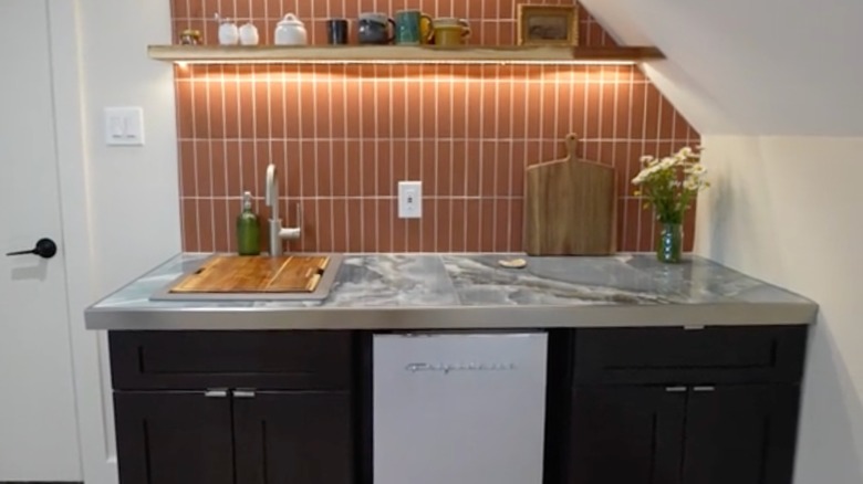 Small kitchen with brown tiles on the wall, marble countertops with a metallic trim, and dark brown cabinets.