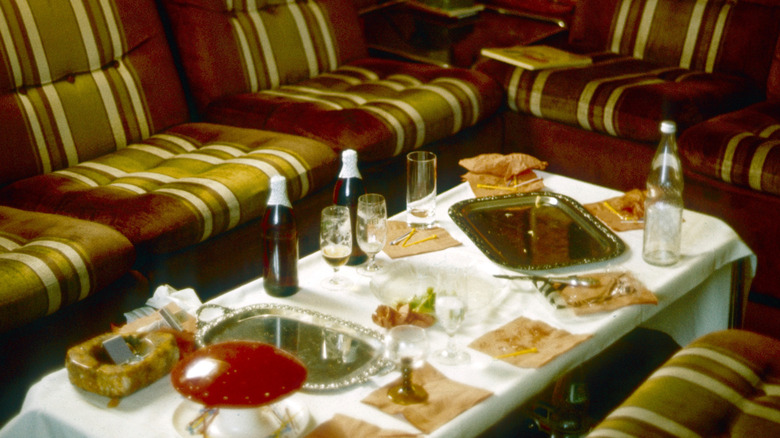Vintage party table scene with bottles, trays, glasses, and napkins on a cocktail table surrounded by seating.