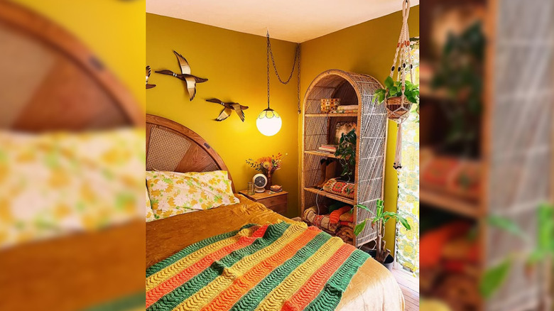 A 1970s-inspired bedroom with striped blanket, floral pillowcases, and arch-shaped rattan shelf.