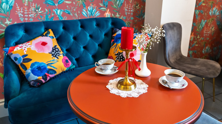 A blue sofa with floral print pillow and floral wallpaper.