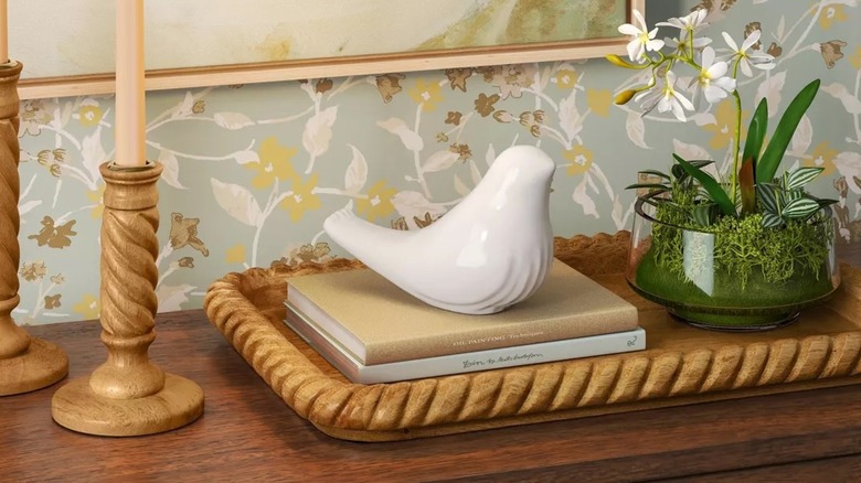 A white ceramic bird figurine on top of some books and next to a plant and candlesticks on a console table.