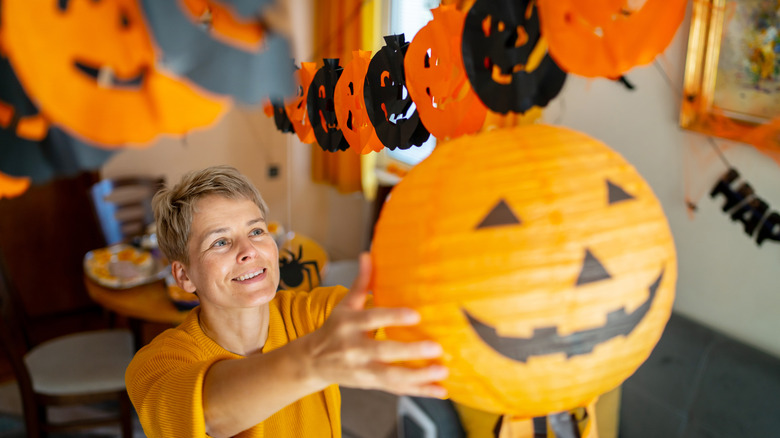 a person hanging up a jack-o'-lantern paper lanterns near a matching paper garland