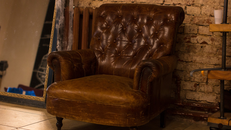 vintage club chair with distressed seat against a brick wall
