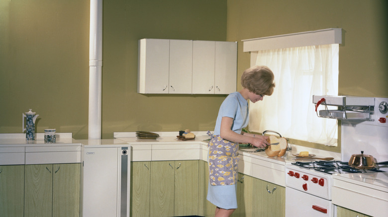 Woman in a 60s kitchen, buttering a loaf of bread.