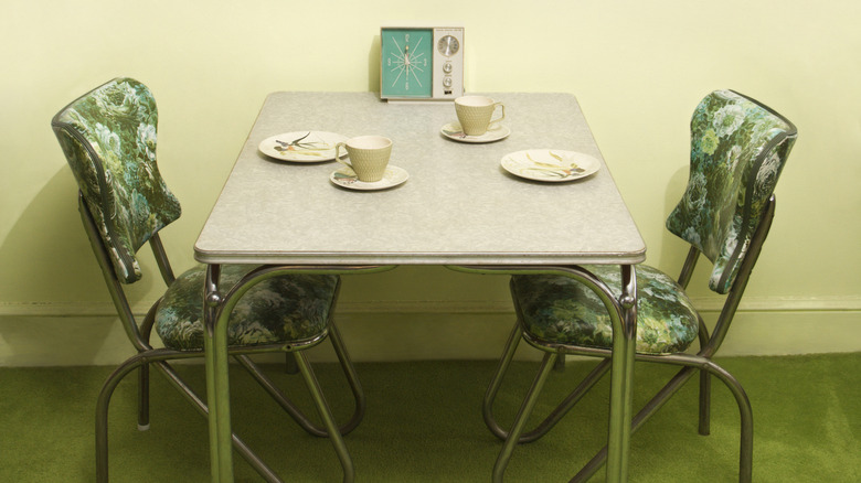 Set of green chairs sitting at a classic Formica table, teacups and matching plates.
