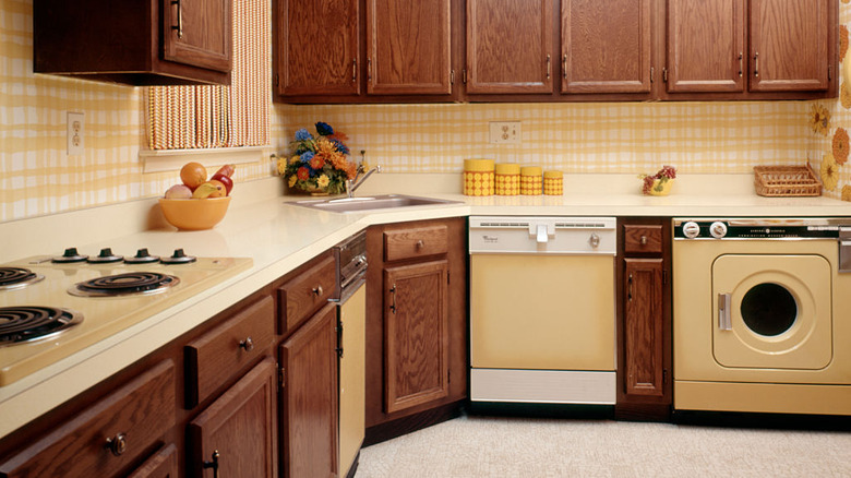 A kitchen in the 1970s with wood cabinets and checkered wallpaper