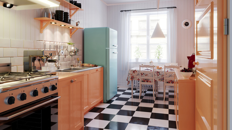 A brightly-lit kitchen with black and white checkered flooring, wood-toned cabinets, and a teal refrigerator.