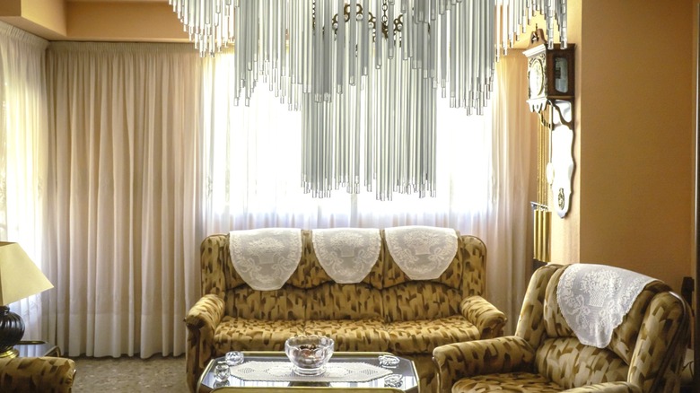 Vintage 1980s living room with patterned chairs, a glass coffee table, and a glass chandelier.