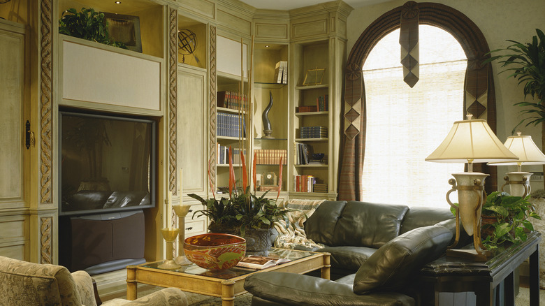 Lavish 1990s living room with leather sofa, arched window, and built-in shelves full of decor