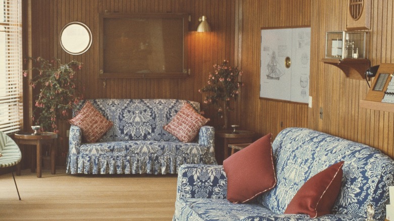 Living room area from an '80s home featuring couches covered with blue floral prints and wood paneling on the walls