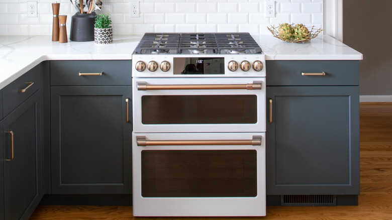 Kitchen with white oven with gold hardware nestled between green-blue cabinets