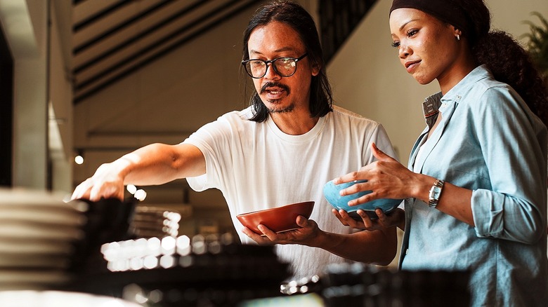 Two people holding ceramic bowls and looking at a stack of other dishes