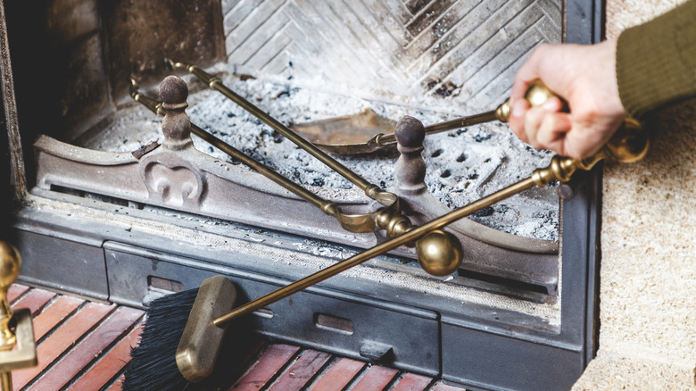 brass fireplace tools being used to clean out ash from a fire