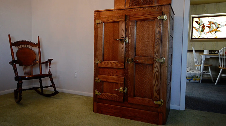 A antique wooden icebox being use as a storage cabinet in a living room.