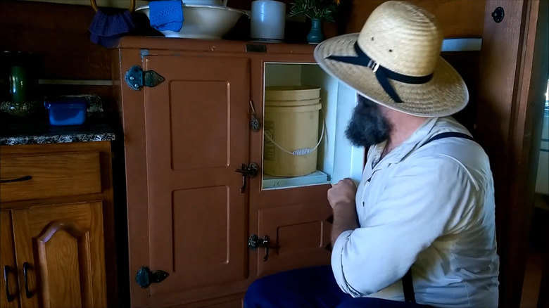 A man demonstrating how to use a 100-year old icebox in a modern kitchen.