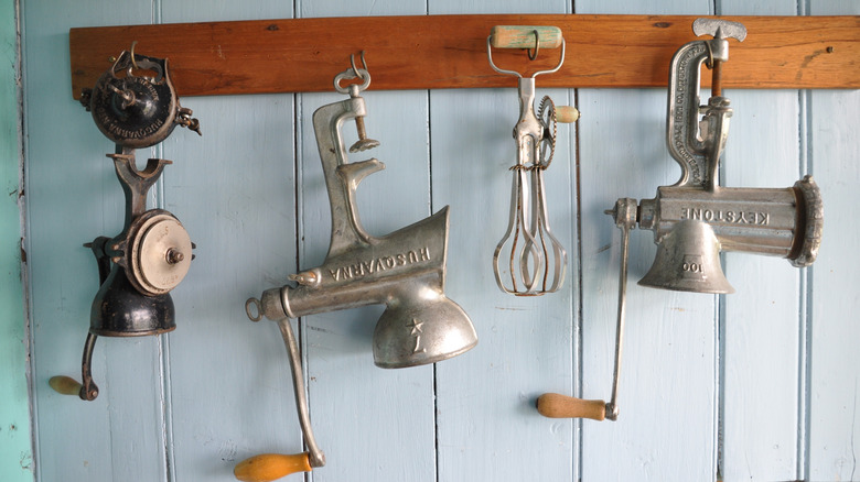 Several silver antique meat grinders hanging on wall hooks