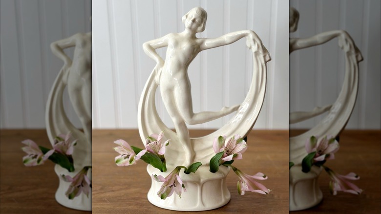 A white dancing lady flower frog vase with pink flowers in its base