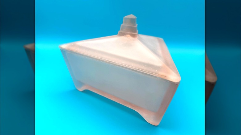 A pink triangular Art Deco style Ramses glass jar photographed on a turquoise background