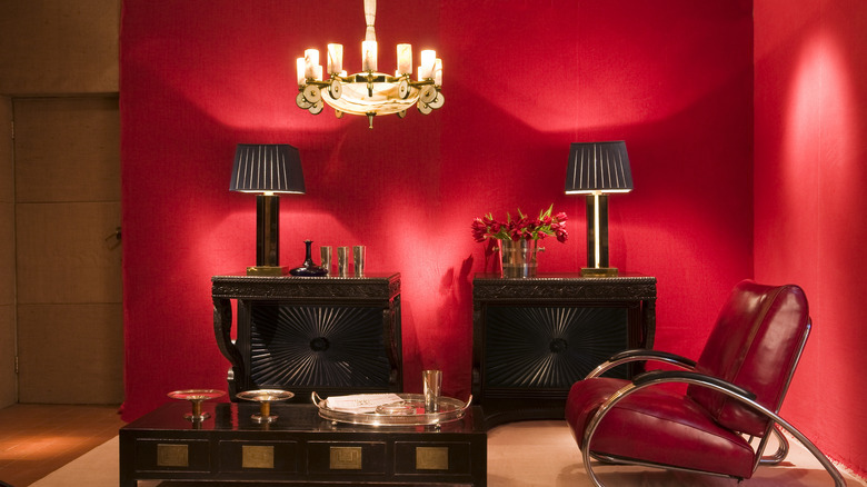 A red-walled living area with a retro red leather chair and dark wood coffee table and other Art Deco furniture.