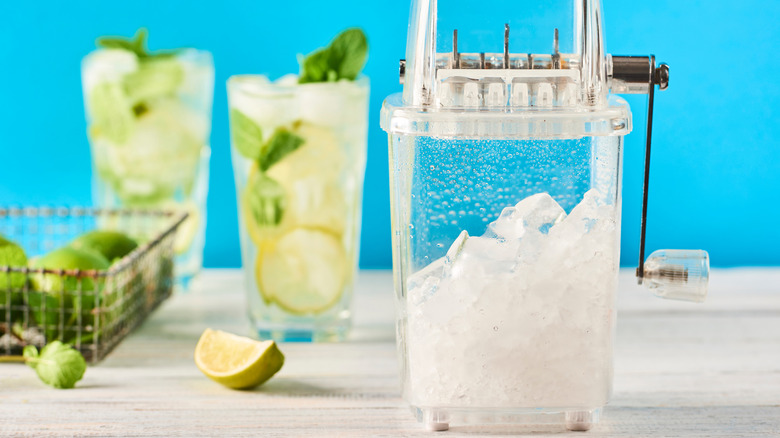 a manual ice crusher with drinks in glasses in the background