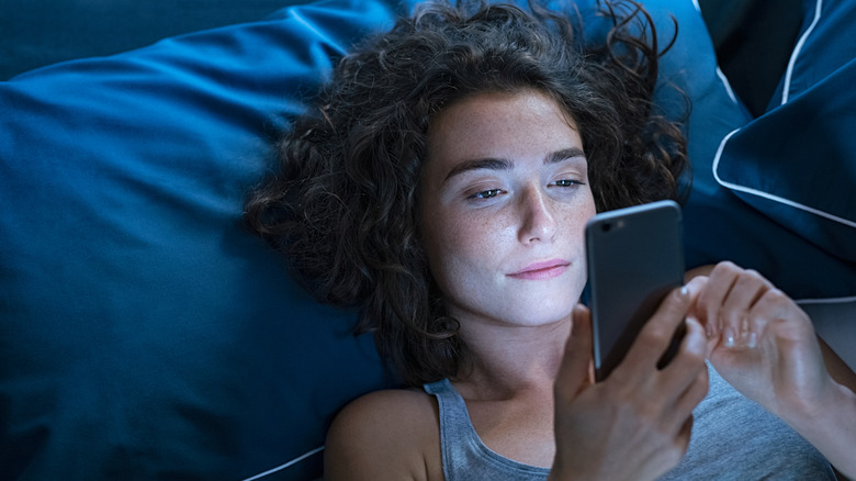 A woman looking at her smartphone while lying in bed.