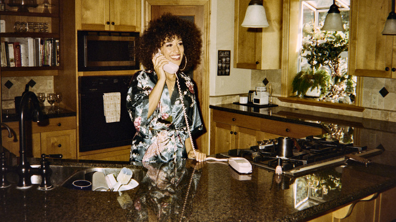 A woman in the 1980s talking on a landline telephone in the kitchen.