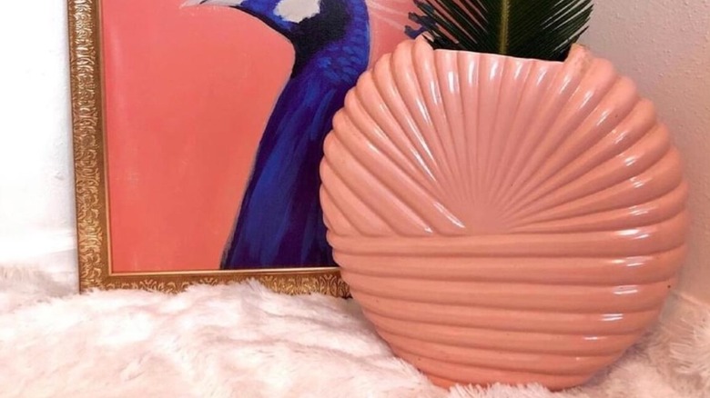A pink vintage Art Deco Revival vase set on a fluffy rug next to a painting of a peacock.