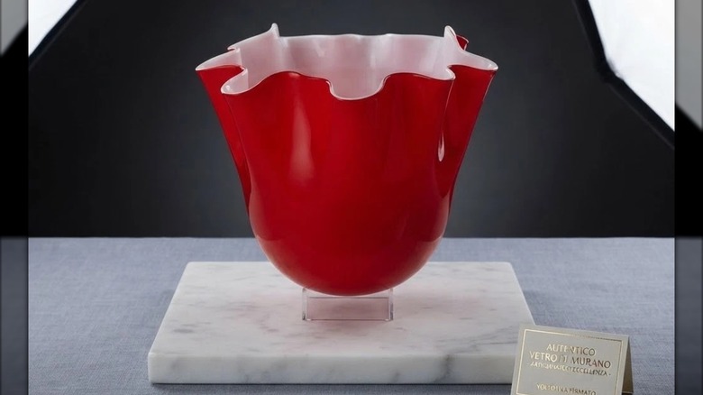 An authentic Murano handkerchief vase with a red exterior and white interior standing next to a certificate of authenticity