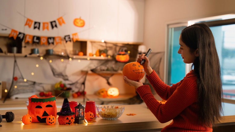 A woman decorating a pumpkin for Halloween with wall decor in the background