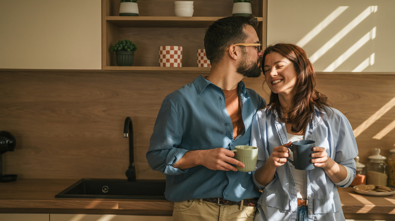 A couple holding coffee cups in their kitchen