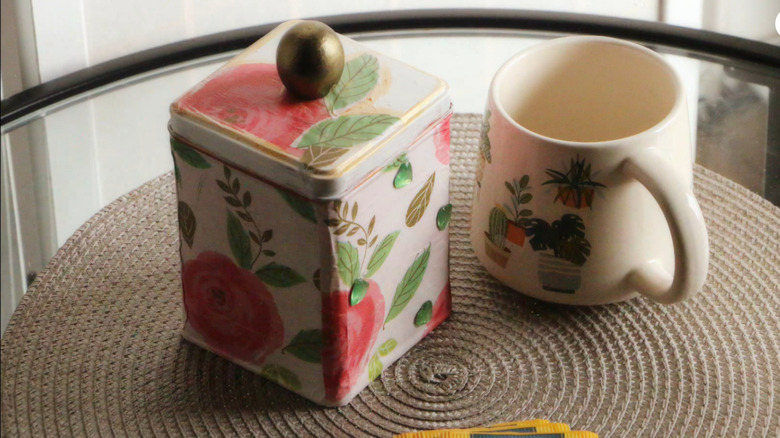 The decorated tea tin next to an empty mug