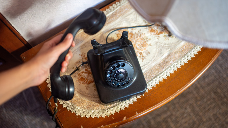 A person holding a rotary phone on a small tabletop