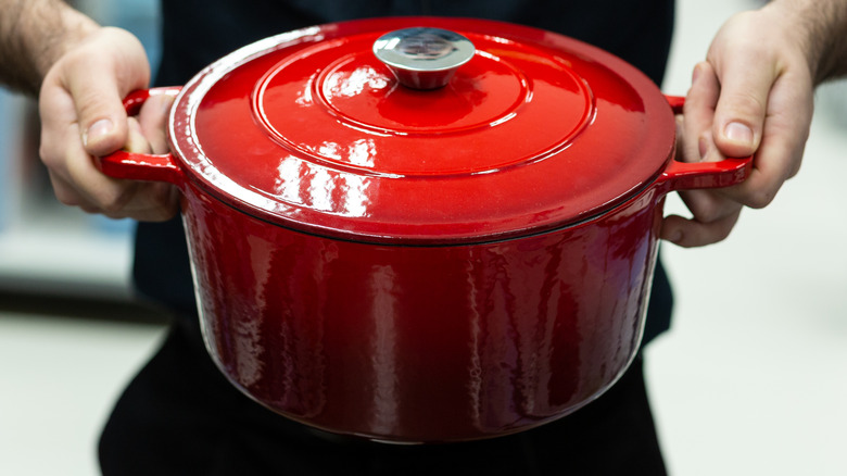 A person holding a red Dutch oven.