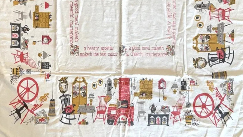 A vintage 1950s tablecloth with a kitschy design featuring furniture and cutesy sayings.