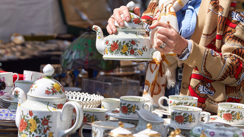 Woman in scarf and patterned jacket holds a tea set at an open-air market